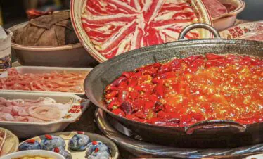 Hotpot, chongqing day tour, chinatrip, Large hot pot with a fiery red broth and chopped chilies, surrounded by raw meats and side dishes for a communal meal.