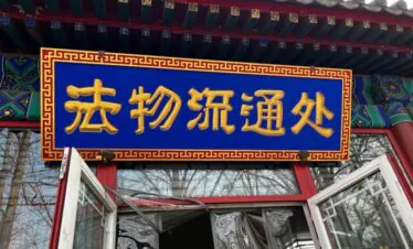 Yonghe Temple official Spiritual Gift Shop, beijing, chinatrip, Blue sign with gold Chinese characters mounted above an open doorway in a traditional Chinese building surface decorate with red trim and ornate frame.
