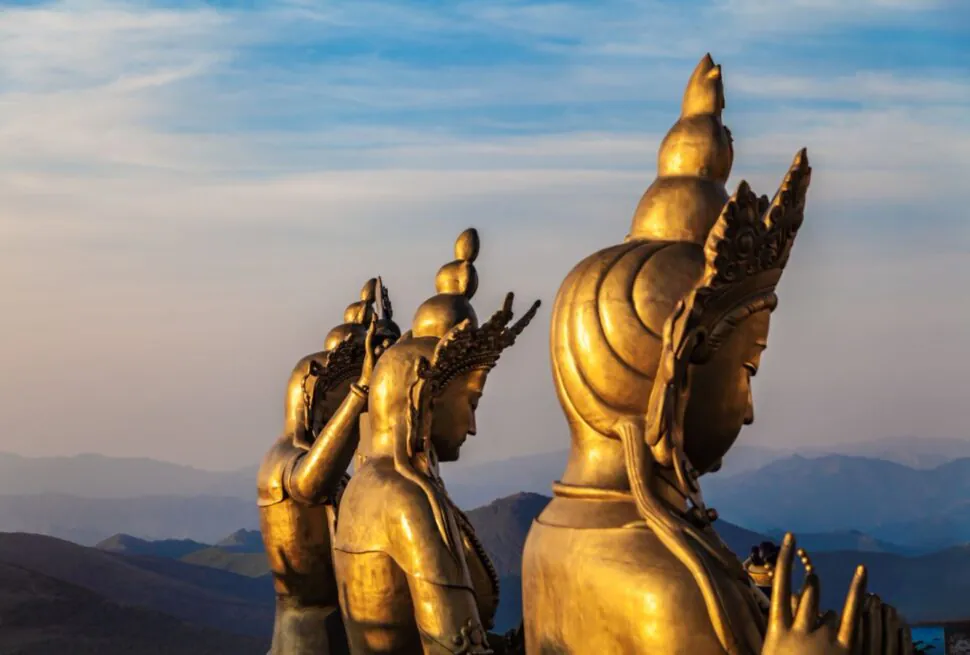 wutai, chinatrip, Row of large golden Buddha-like statues on a mountain ridge at sunset, with blue sky and distant hills in the background.