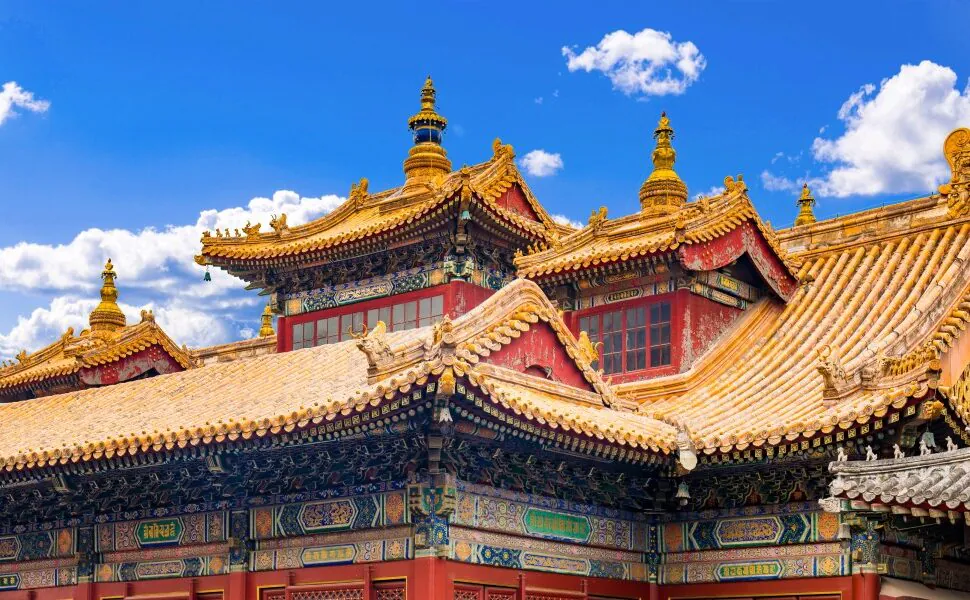yonghe temple, beijing, chinatrip Colorfully decorated temple roof with golden tiles and ornate carvings beneath a bright blue sky.