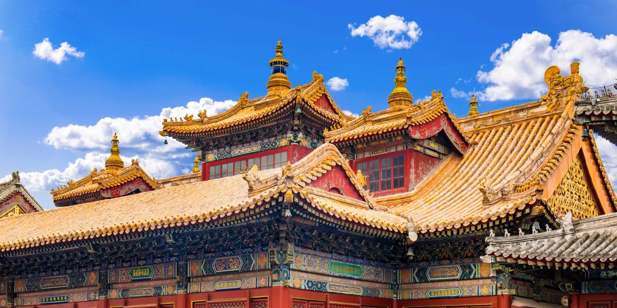 yonghe temple, beijing, chinatrip Colorfully decorated temple roof with golden tiles and ornate carvings beneath a bright blue sky.