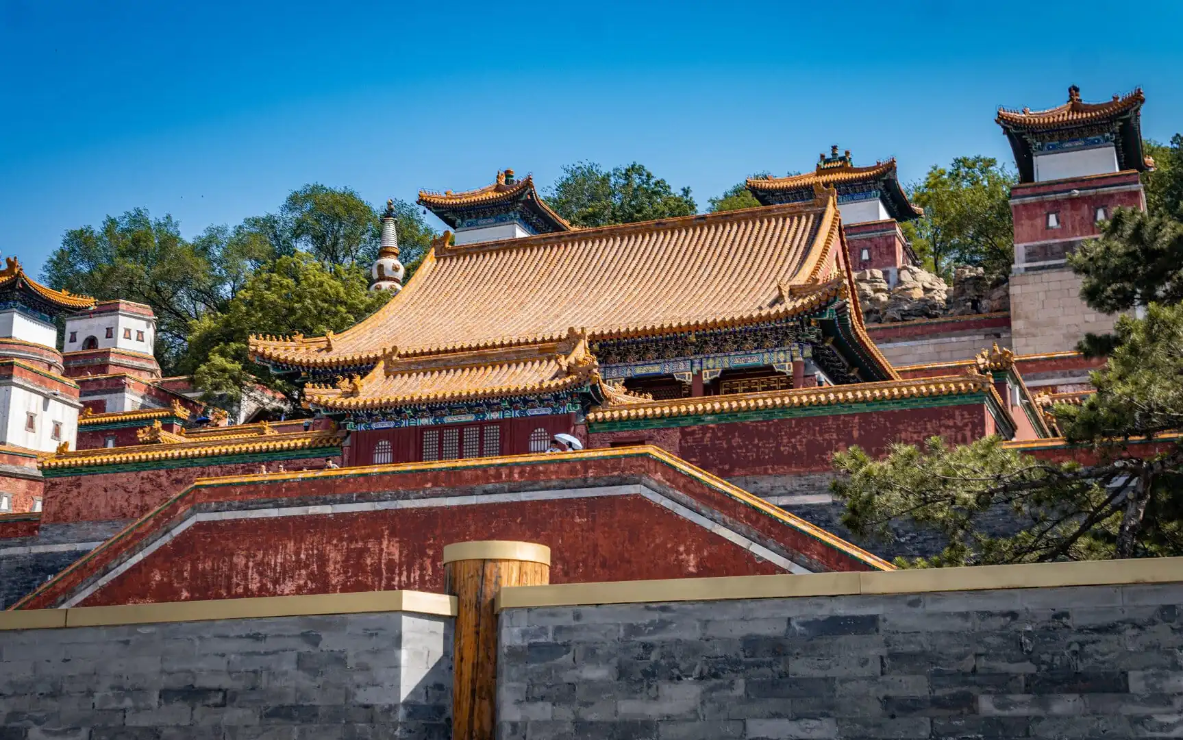 The Summer Palace,Beijing,Chinatour Traditional Chinese temple complex with ornate yellow-tiled roofs, red walls, and blue sky background on a hillside area of trees and stone walls.