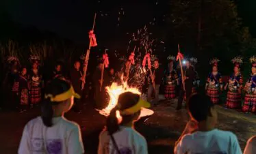 School trip in Guizhou, chinatrip, Group of people in colorful traditional costumes standing around a blazing bonfire at night, sparks flying from the flames.