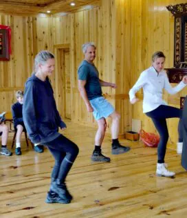 School trip in Guizhou, chinatrip, Group of people in a wooden studio dancing or practicing; a man at the far right plays a traditional erhu instrument while others watch or join in.