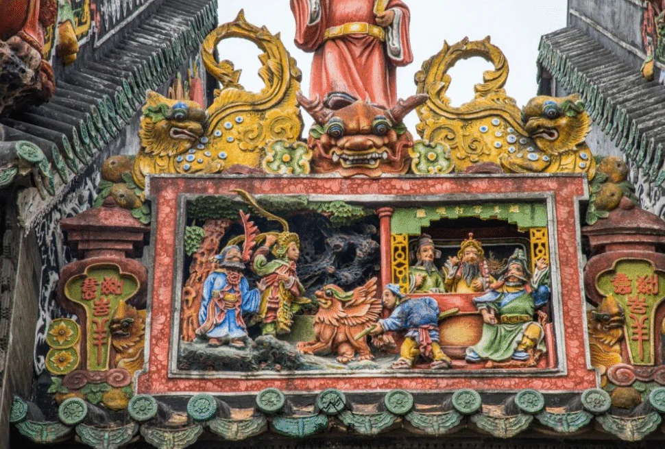 Historical Landmarks & Culinary Delights,Guangzhou,Chinatour Colorful carved temple panel with figures around a central dragon and mythic creatures, ornate green tiled roof edges of a traditional roof.