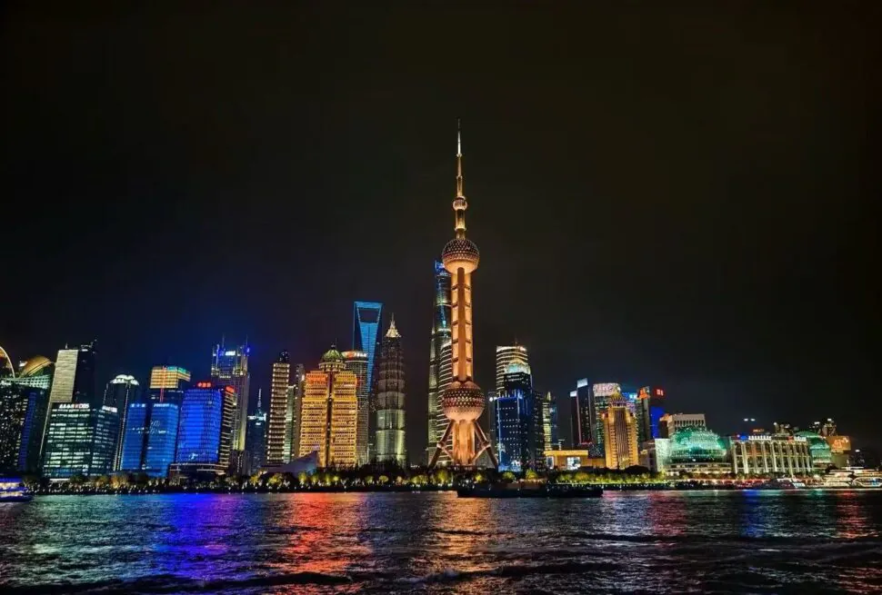 Night view of Shanghai skyline along the Huangpu River, with the Oriental Pearl Tower lit up on the horizon.