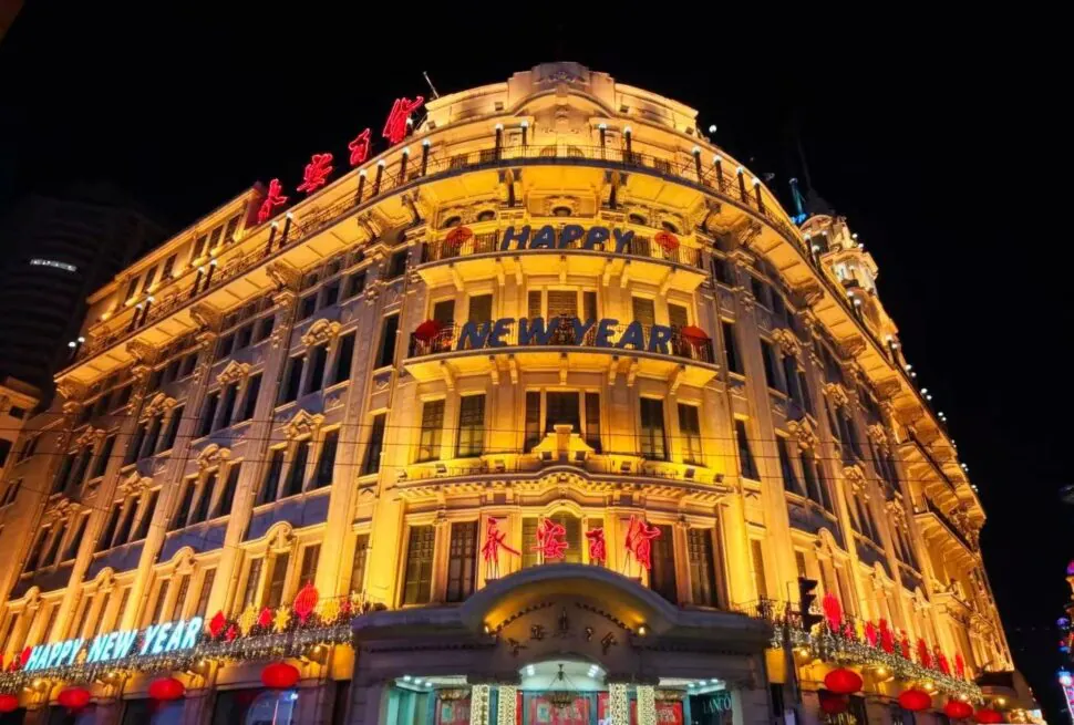 Nanjing Road,Chinatour Ornate night-time building facade lit in warm yellow lights with 'Happy New Year' banners and red lanterns outside.