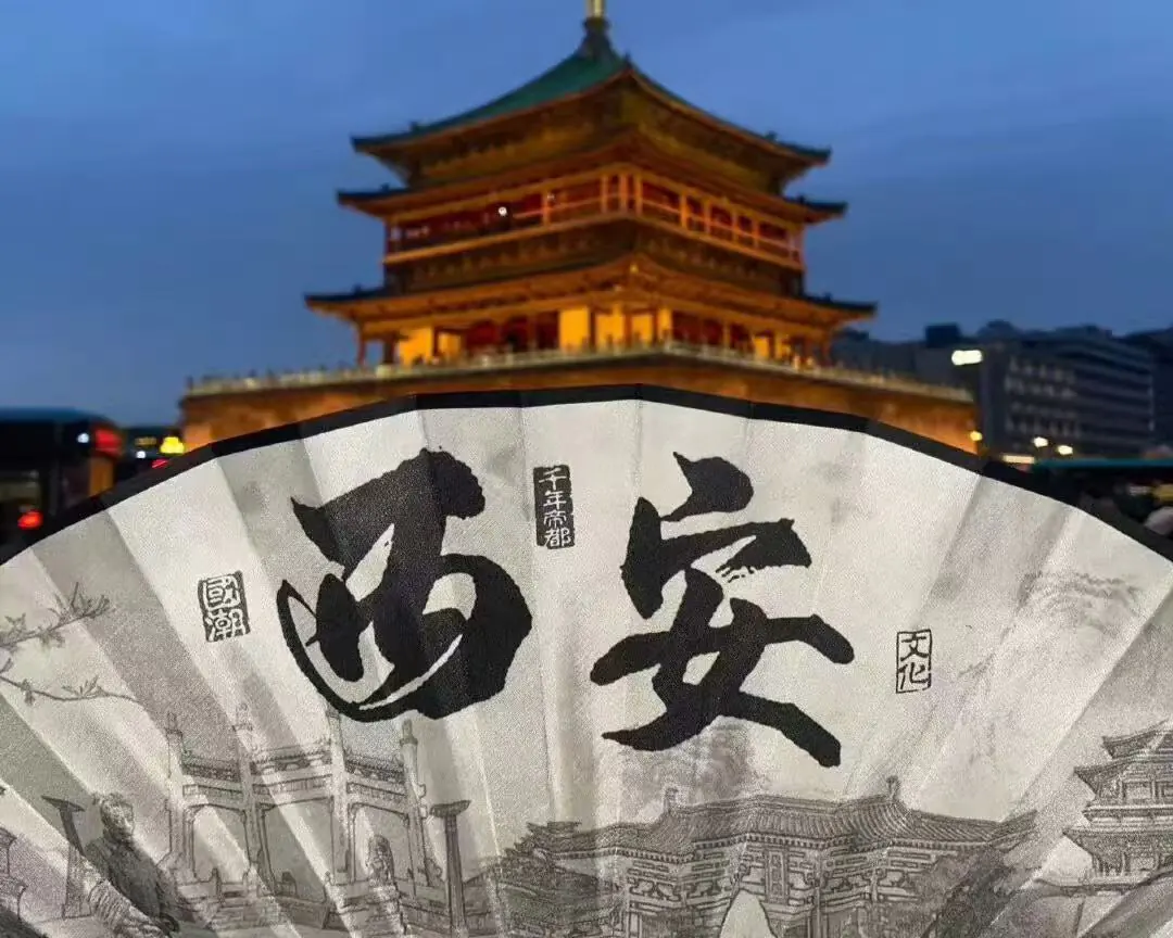 Night scene with a lit multi-tier Chinese pagoda behind a large decorative fan featuring bold calligraphy and ink drawings in the foreground.