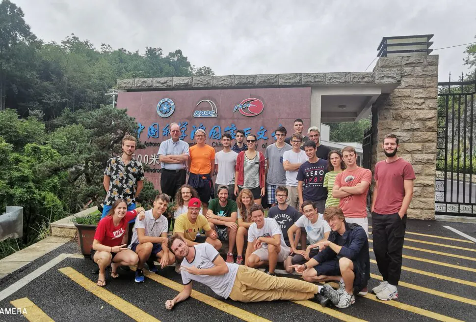 guizhou's FAST, chinatrip, A large group of students and a few adults posing for a group photo outside an institute entrance sign, with greenery and a black metal gate in the background.