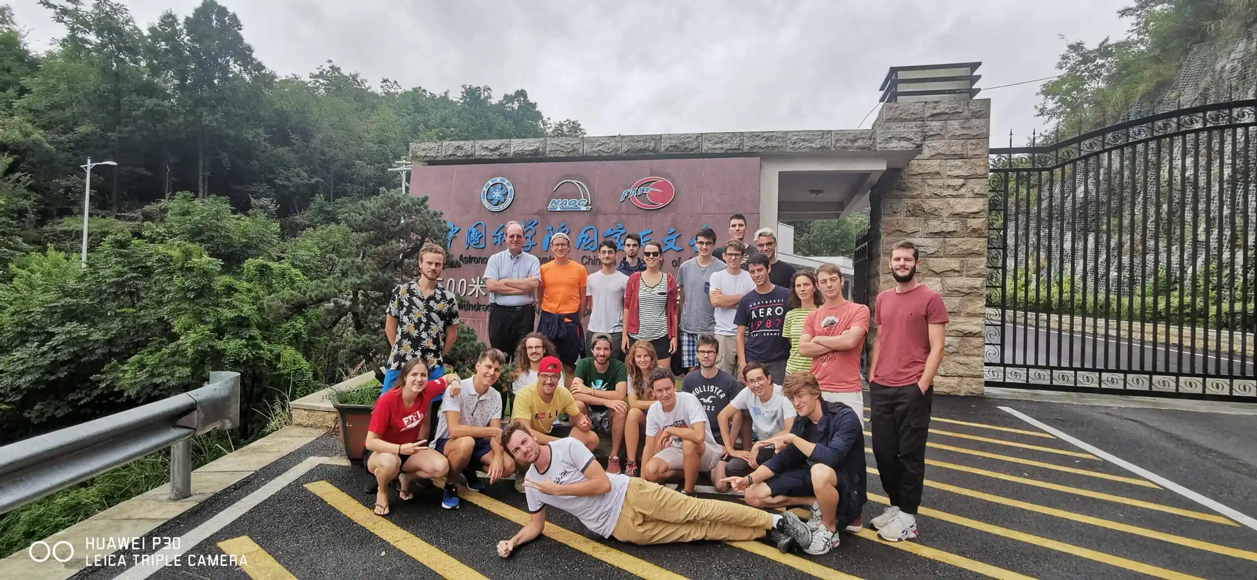 guizhou's FAST, chinatrip, A large group of students and a few adults posing for a group photo outside an institute entrance sign, with greenery and a black metal gate in the background.
