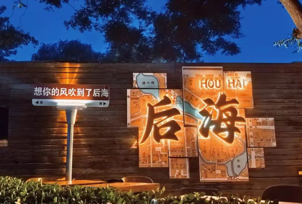 Houhai Bar Street,Beijing,Chinatour Night scene of a wooden wall with an illuminated map-marts art piece featuring large glowing Chinese characters, against a dark blue evening sky. or Wooden wall installation with a lit multi-panel map and big illuminated Chinese characters, in a nighttime setting.