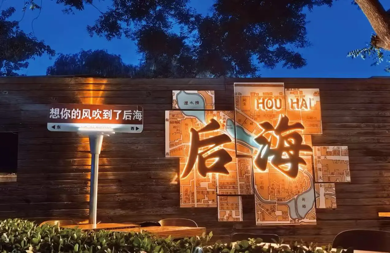 Houhai Bar Street,Beijing,Chinatour Night scene of a wooden wall with an illuminated map-marts art piece featuring large glowing Chinese characters, against a dark blue evening sky. or Wooden wall installation with a lit multi-panel map and big illuminated Chinese characters, in a nighttime setting.