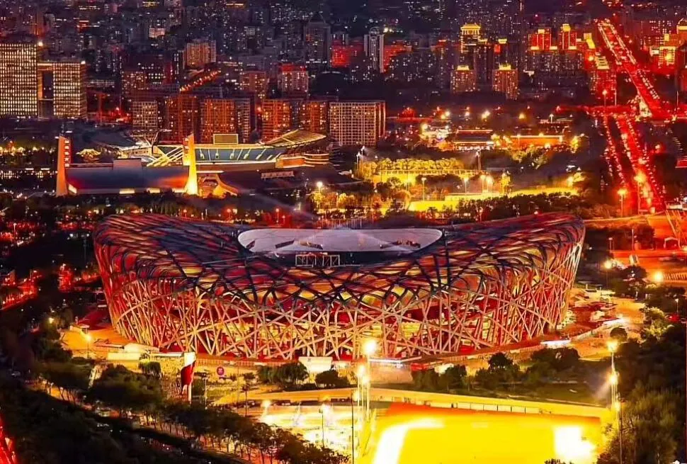 Olympic Forest Park,Beijing,Chinatour Night aerial view of the Beijing National Stadium (Bird's Nest) illuminated in red and orange, with city lights in the background.