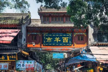 Xi'an Muslim Quarter,Chinatour Decorative Chinese gateway over a bustling market street with shops and stalls beneath a blue sign panel and ornate roof.