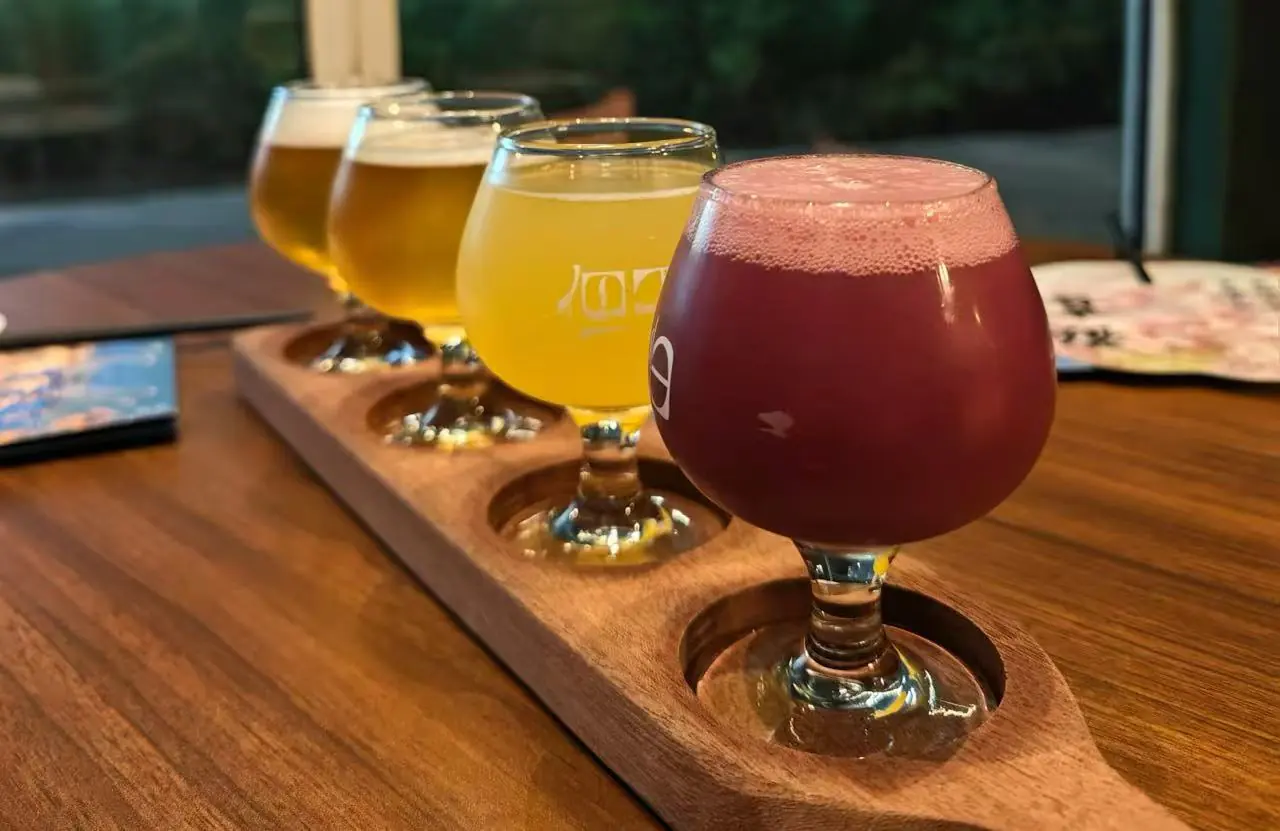 Sanlitun Bar Street,Beijing,Chinatour Beer flight on a wooden paddle with four snifter glasses, foreground filled with a dark reddish beer and foamy head, in a bar setting.