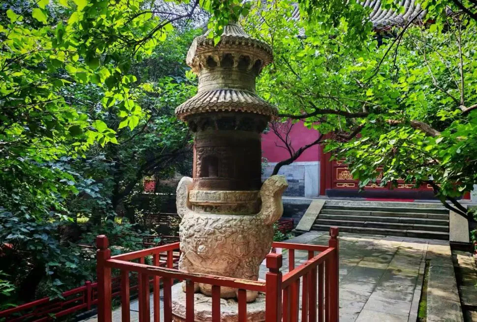 Stone dragon-topped lantern in a lush garden surrounded by red railing and stone steps to a temple door behind.
