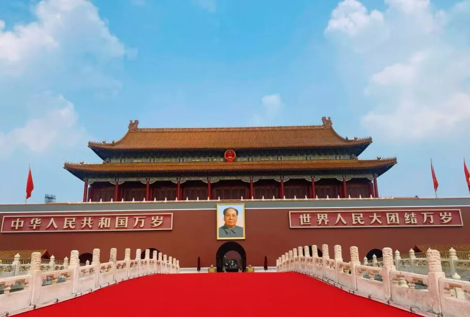 Tiananmen Gate in Beijing with Mao Zedong portrait, red banners, and a long red carpet leading to the entrance.