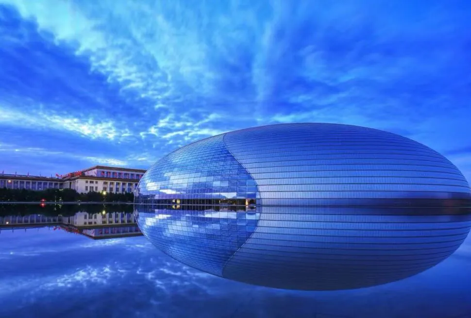 Beijing National Centre,Chinatour National Centre for the Performing Arts (the Egg) reflected in a calm pool under a blue sky with surrounding buildings and trees.