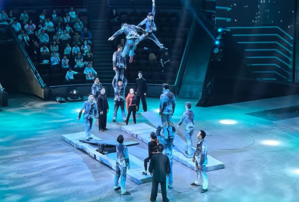 Shanghai Acrobatics Show,Shanghai,Chinatour Acrobat troupe performs an aerial stunt on elevated platforms in a circular arena, with audience watching from stands in blue lighting.