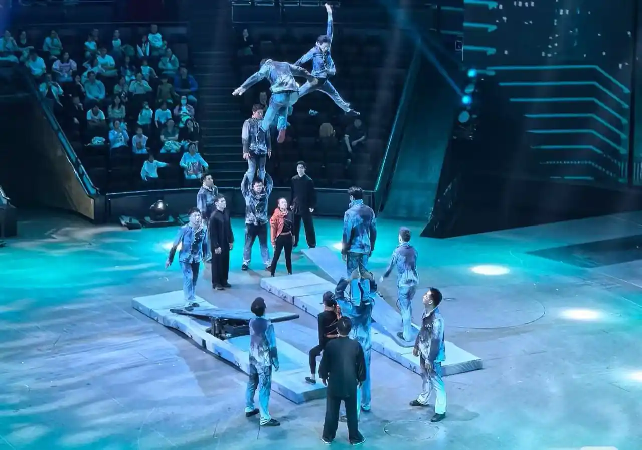 Shanghai Acrobatics Show,Shanghai,Chinatour Acrobat troupe performs an aerial stunt on elevated platforms in a circular arena, with audience watching from stands in blue lighting.