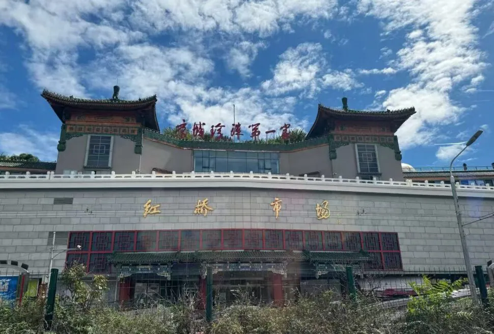 Front view of a building with traditional Chinese pagoda-style roofs, gold Chinese characters on the wall, and red-windowed doors beneath a blue sky.