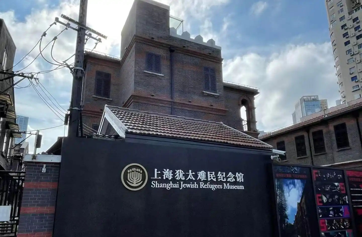 Jewish Refugees Museum,Shanghai,Chinatour Exterior view of the Shanghai Jewish Refugees Museum with a dark wall sign displaying the museum name in Chinese and English behind a brick building.