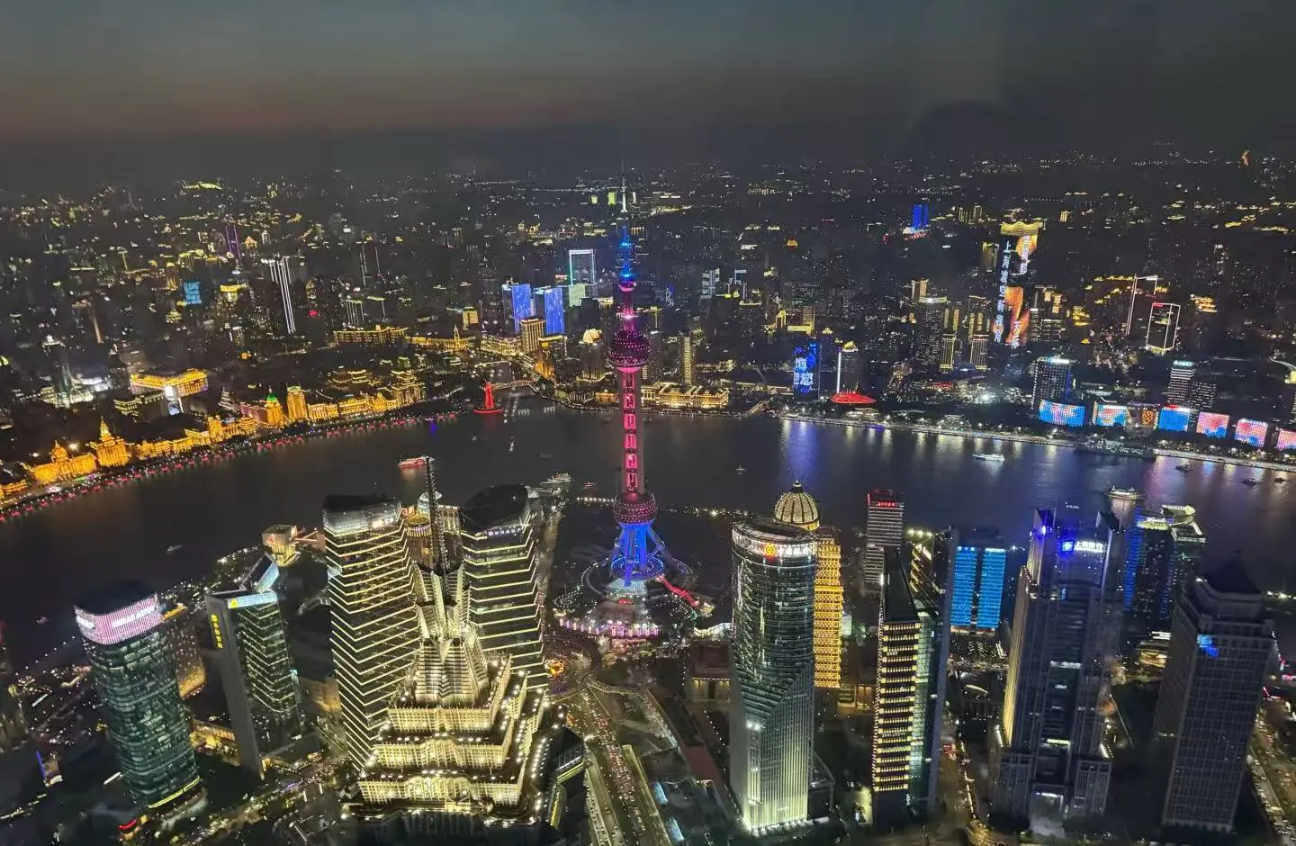 Shanghai World Financial Center,Shanghai,Chinatour Night aerial view of Shanghai's illuminated skyline along the Huangpu River, featuring the brightly lit Oriental Pearl Tower in the center.