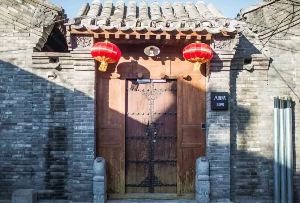 Traditional Chinese wooden door set in a grey brick wall, with red lanterns hanging above the entrance.