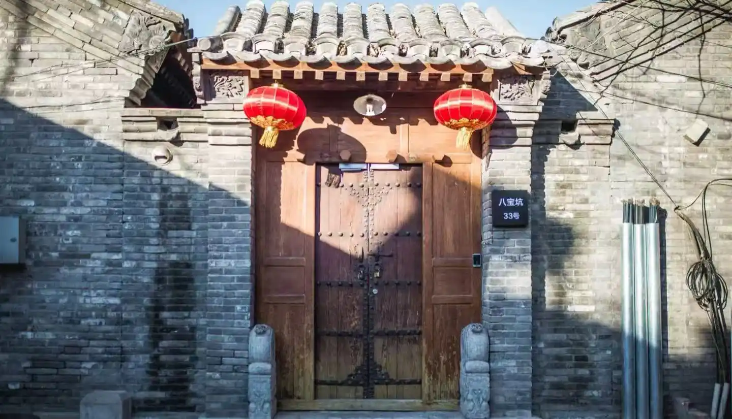 Beijing's Hutongs,Chinatour Traditional Chinese wooden door set in a grey brick wall, with red lanterns hanging above the entrance.