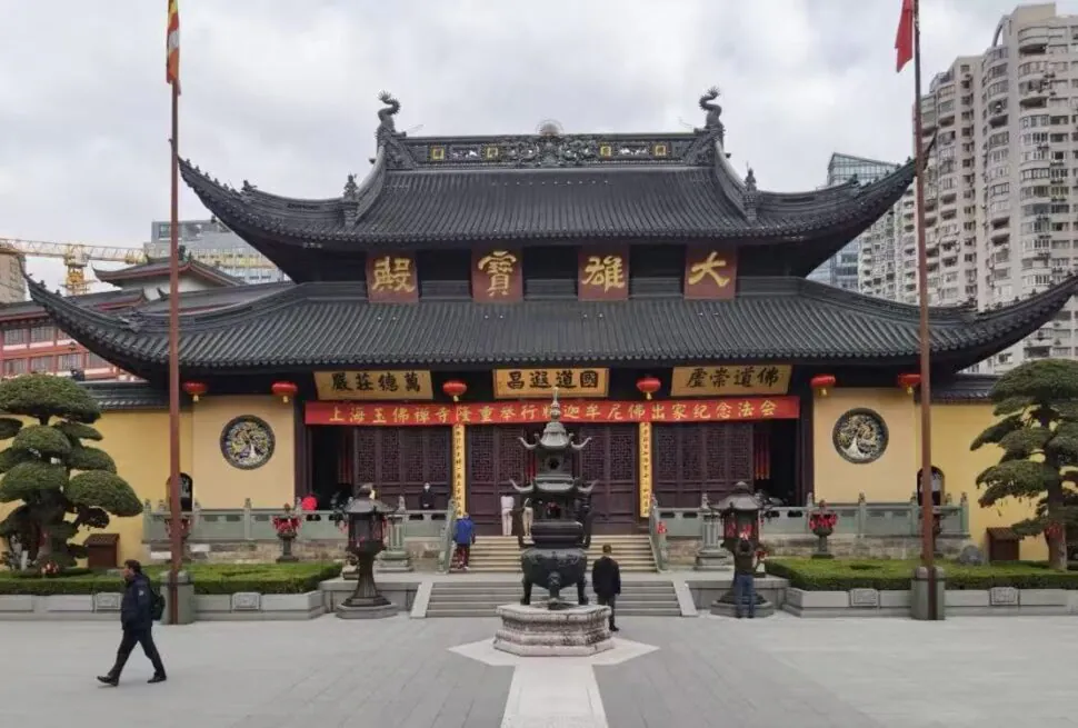 Shanghai Jade Buddha Temple,Shanghai,Chinatour Traditional Chinese temple with ornate curved roof and red lanterns in a courtyard, urban high-rises in the background.