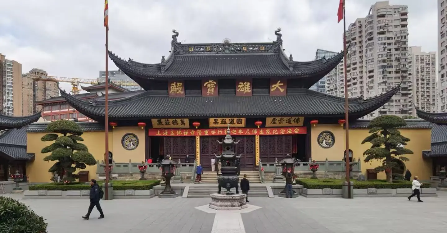 Traditional Chinese temple with ornate curved roof and red lanterns in a courtyard, urban high-rises in the background.