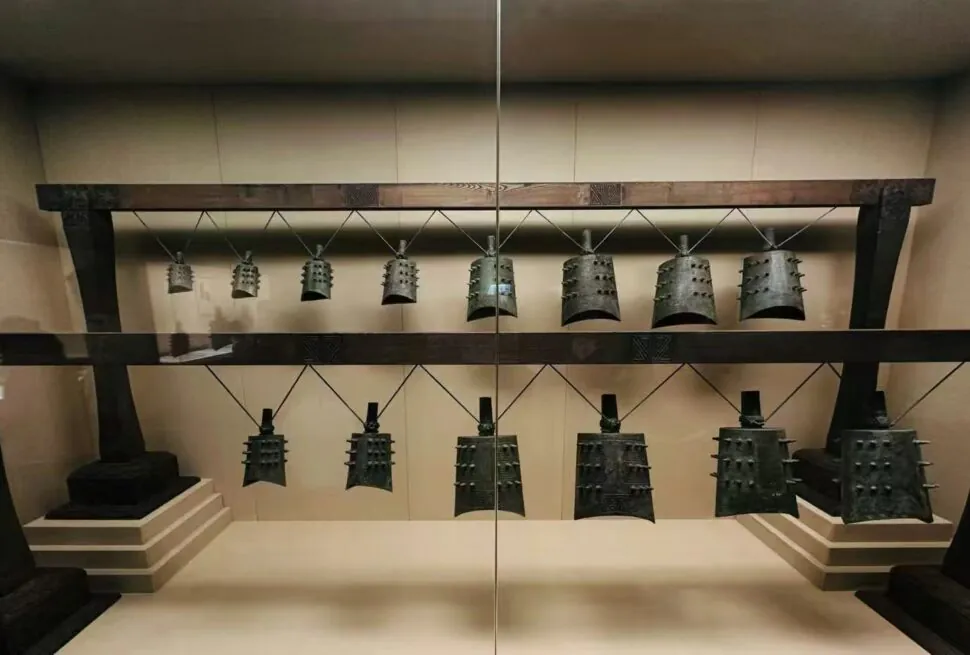 Row of Dalek shells hanging on a rack in a museum display behind glass, arranged in two levels.