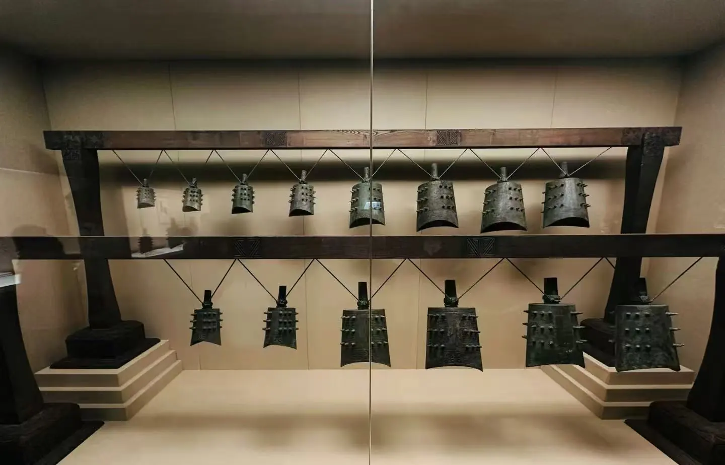 Row of Dalek shells hanging on a rack in a museum display behind glass, arranged in two levels.