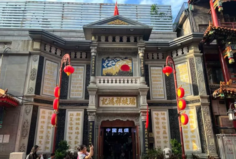 Ornate Chinese temple facade with gold inscriptions, stone columns, and red lanterns along the sides of a central doorway.