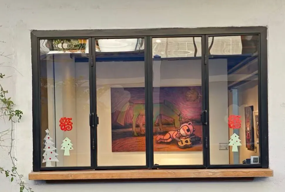 Storefront window with a black frame; inside is a colorful painting of a bear playing a guitar, flanked by holiday paper trees on the glass and red ornaments on the pane.
