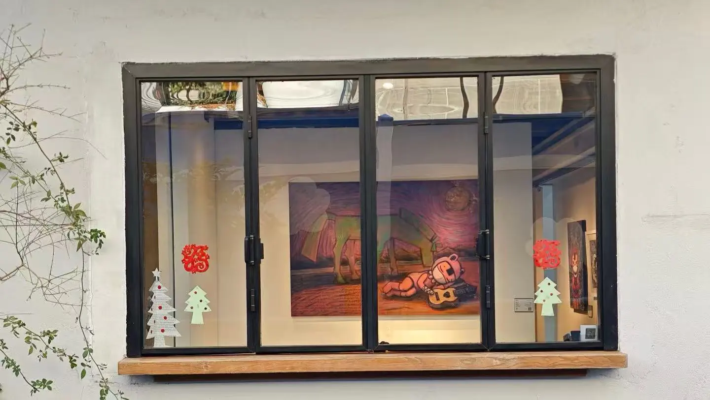 Shanghai M50 Creative Park ,Shanghai,Chinatour Storefront window with a black frame; inside is a colorful painting of a bear playing a guitar, flanked by holiday paper trees on the glass and red ornaments on the pane.