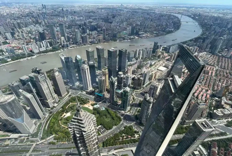 Aerial view of a dense downtown skyline along a wide river, with numerous high-rise buildings and a green park in the foreground.