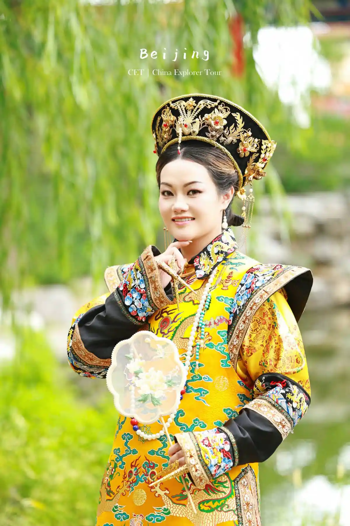 hanfu photoshoot, the forbidden city, beijing, qing dynasty, female, solo, chinatravel, Woman in an ornate yellow traditional Chinese imperial costume with a jeweled headdress, posing outdoors with a decorative fan.