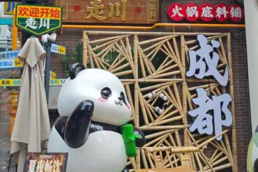 Front of a Chinese hotpot restaurant with a large panda statue holding a green cup, a bamboo lattice facade, and big white Chinese characters on the right.