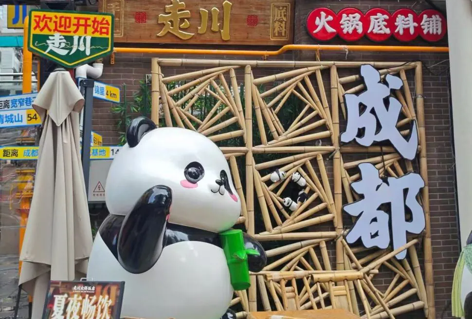 Front of a Chinese hotpot restaurant with a large panda statue holding a green cup, a bamboo lattice facade, and big white Chinese characters on the right.