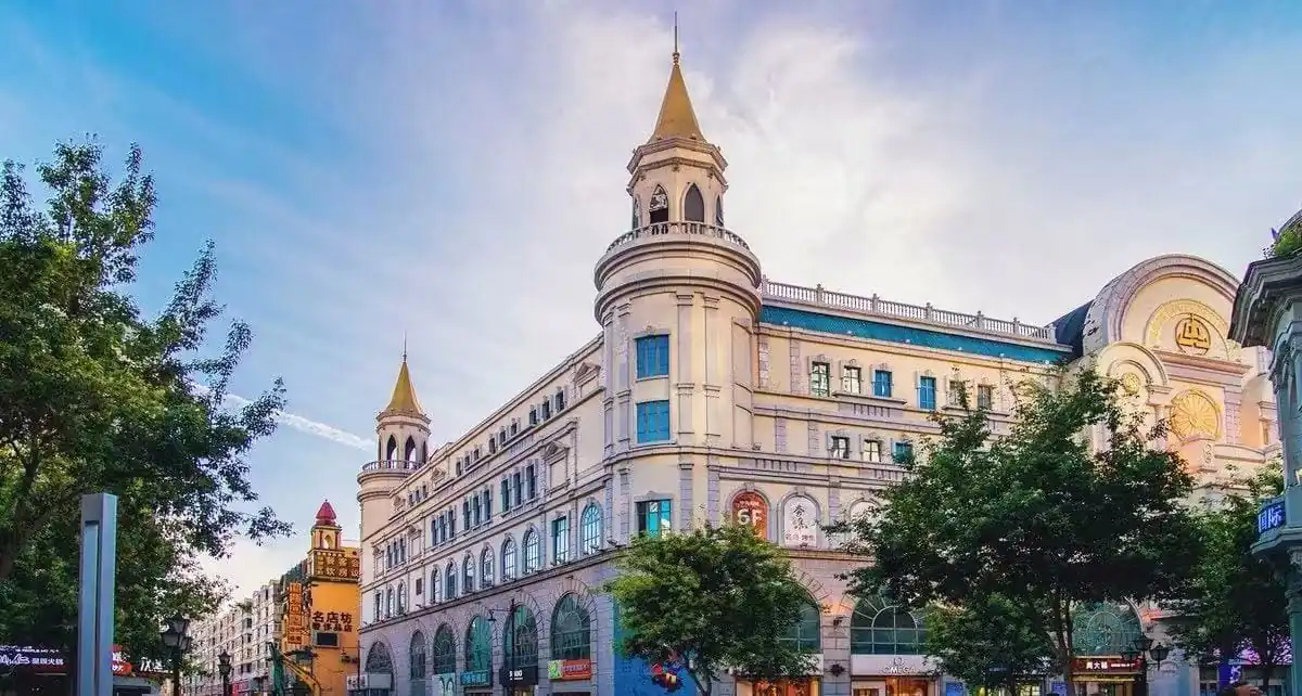 Harbin Central Street,Harbin,Chinatour Historic European-style shopping arcade with two tower spires and arched storefronts along a tree-lined street on a sunny day.