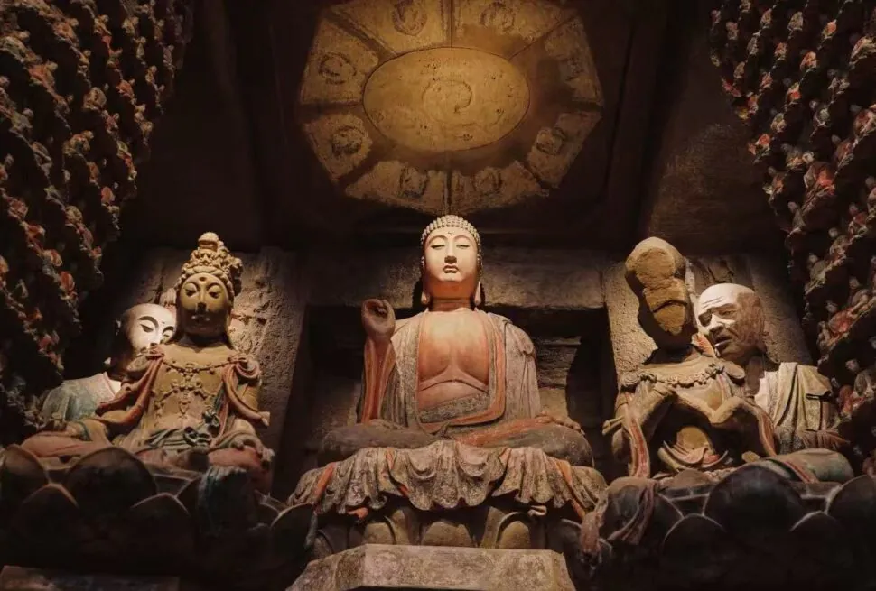 Shaanxi History Museum,Xi`an,Chinatour Central Buddha statue seated in a cave temple with smaller statues around, dimly lit and ancient stone carvings behind it