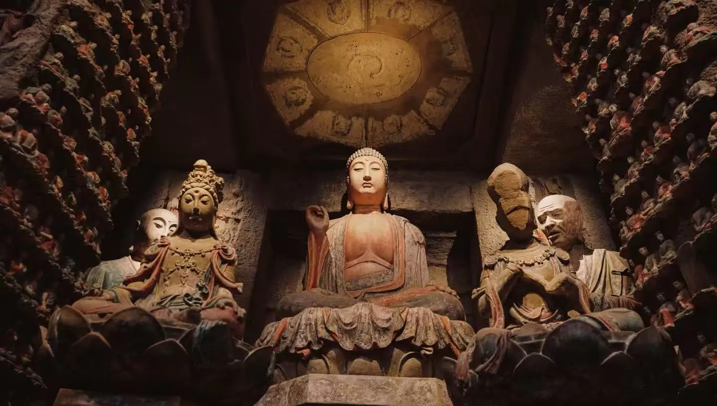 Shaanxi History Museum,Xi`an,Chinatour Central Buddha statue seated in a cave temple with smaller statues around, dimly lit and ancient stone carvings behind it
