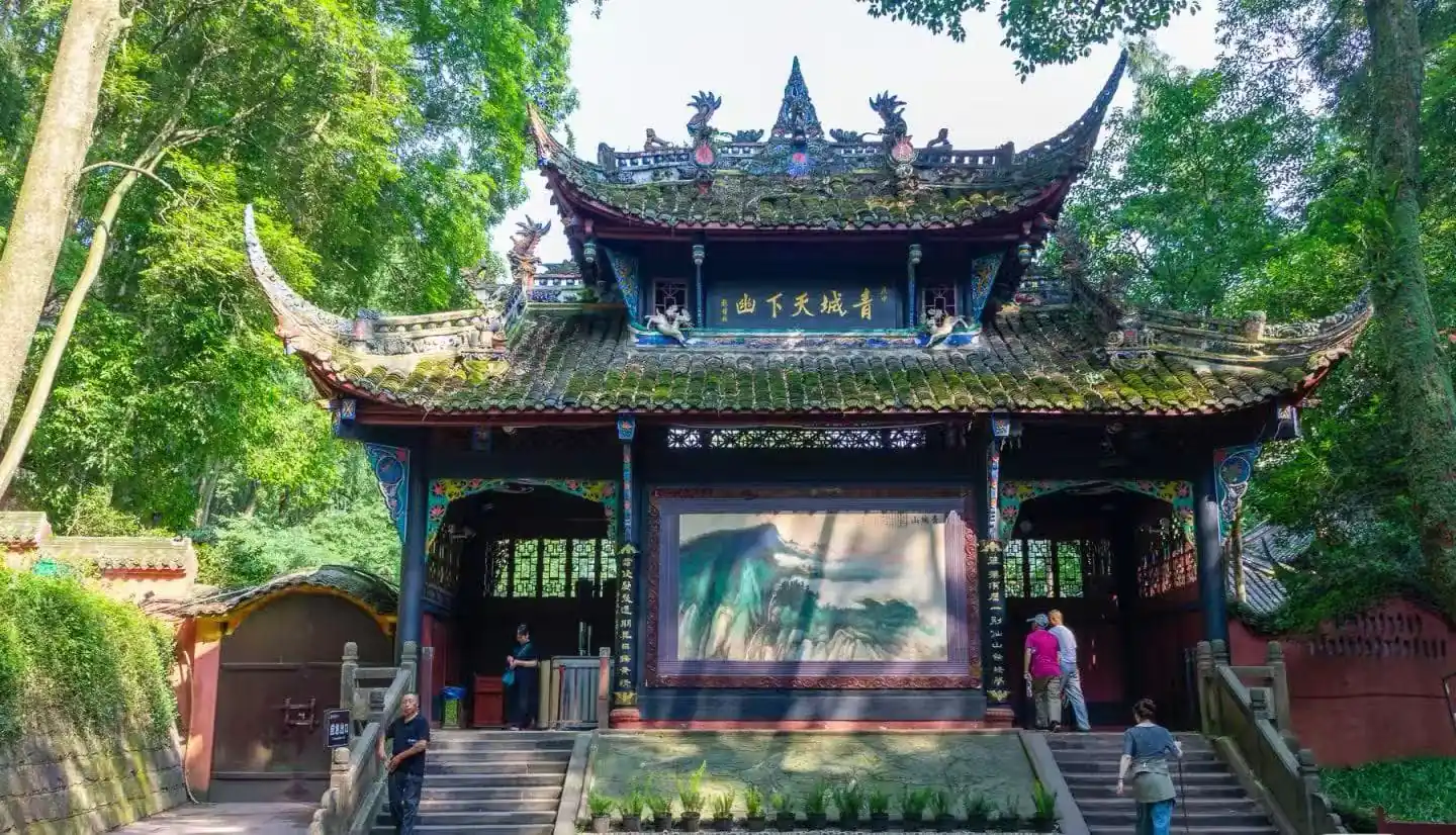 Mount Qingcheng and Dujiangyan,Chengdu,Chinatour Traditional Chinese pavilion tucked in a lush green garden with ornate roof dragons and a large landscape painting displayed inside the open hall, visitors examining the artwork.