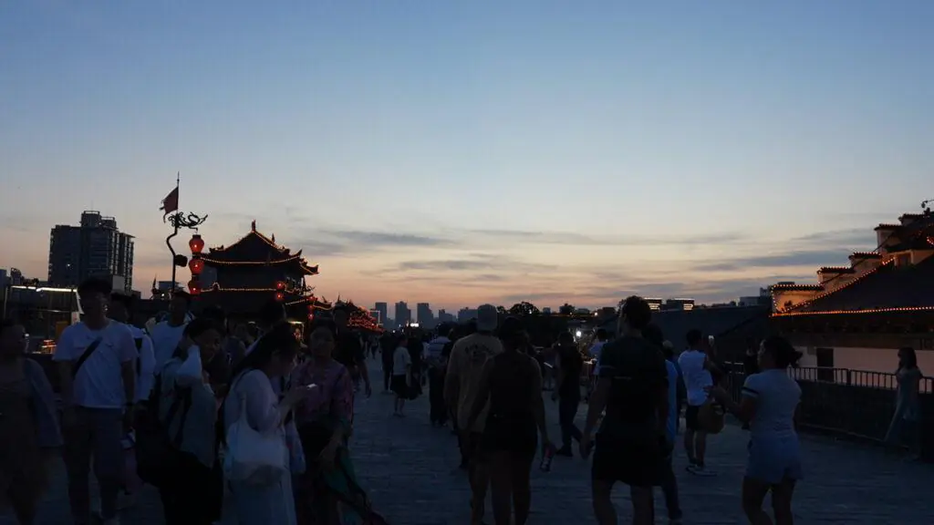 Xi’an City Wall,Xi`an,Chinatour Crowd strolling along a waterfront at dusk, with a pagoda-style building and red lanterns lit along the walkway.