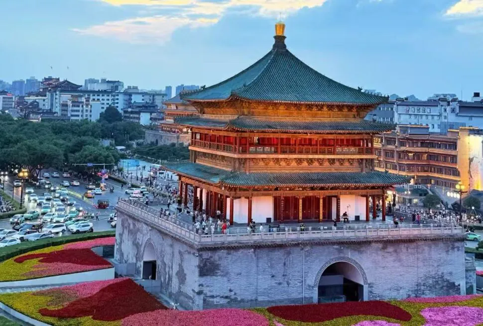 Bell and Drum Tower,Xi`an,Chinatour Traditional multi-tier Chinese pagoda atop a stone fortress overlooking a city, with colorful flowerbeds in the foreground.