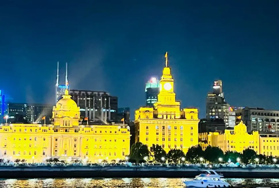 Huangpu River,Shanghai,Chinatour Nighttime cityscape with warmly lit, yellow historic buildings along a river and a white motorboat in the foreground.