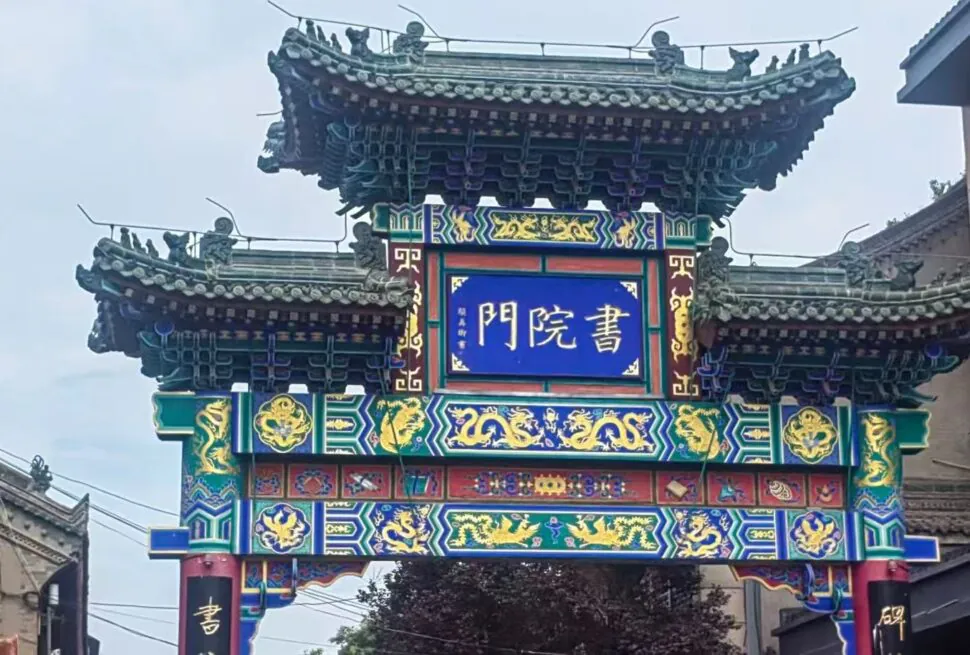 Colorful traditional Chinese paifang with ornate dragons and blue signboard at the center, in a street setting