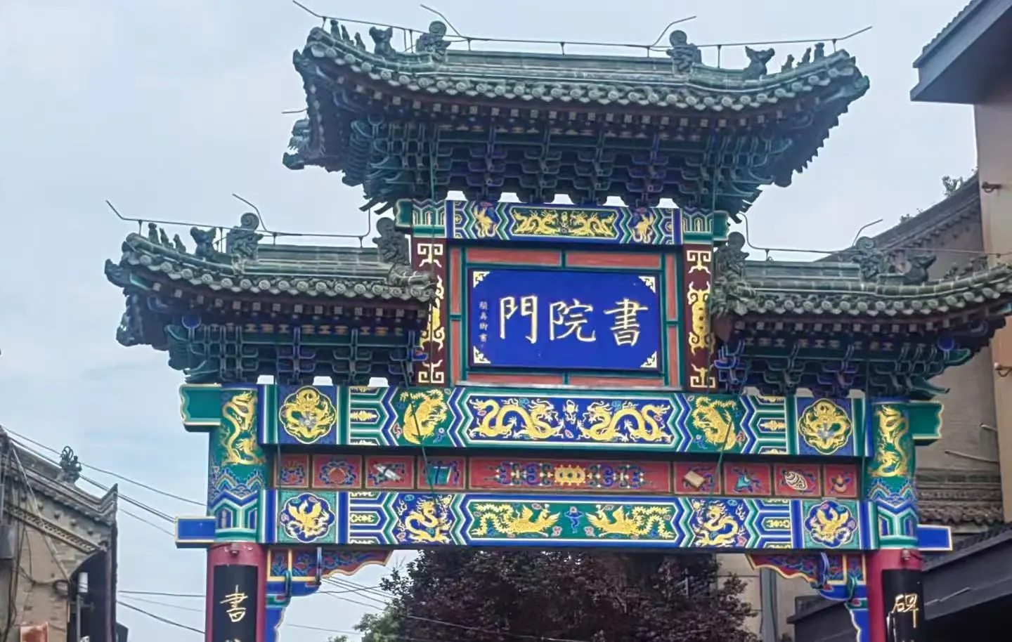 Colorful traditional Chinese paifang with ornate dragons and blue signboard at the center, in a street setting