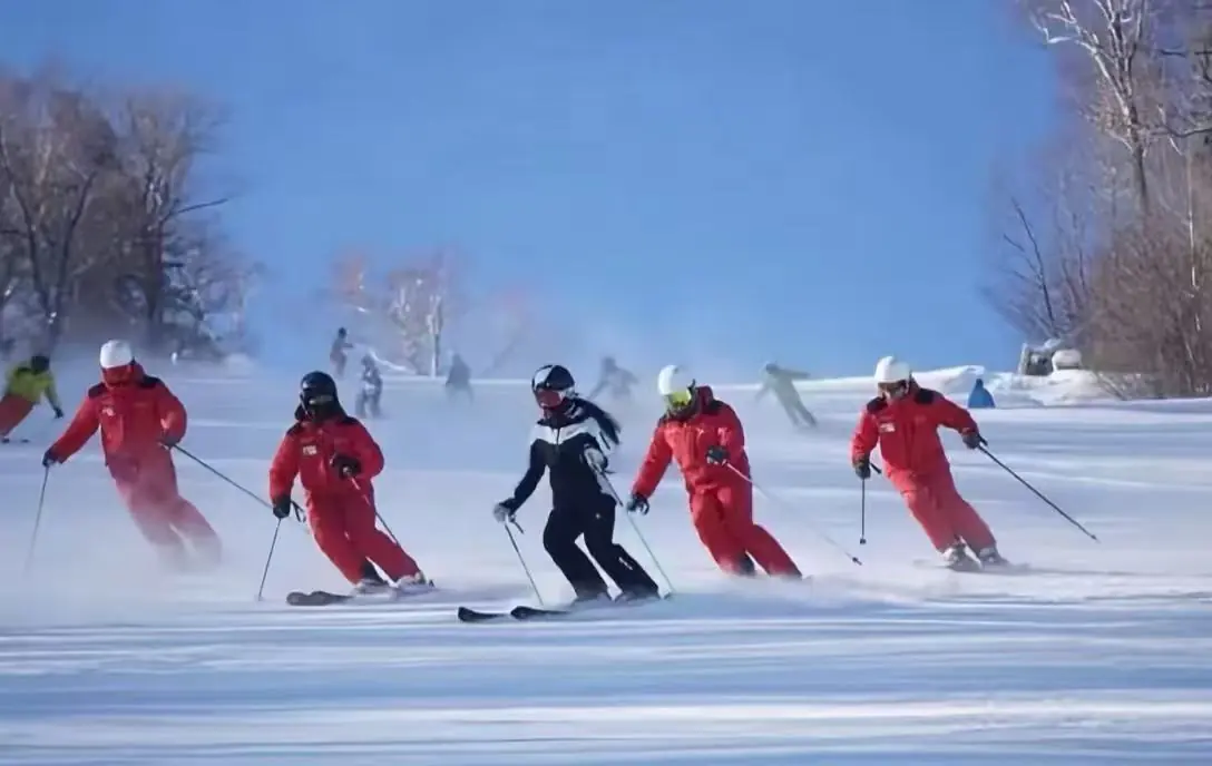 Yabuli Ski Resort,Harbin,Chinatour Group of skiers in red suits carving turns on a sunny snowy slope; a black-clad instructor leads.